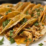Mini tacos de pollo servidos en plato, decorados con salsa y crema agria.