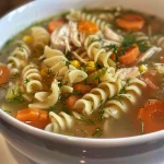 Tazón de sopa cremosa con trozos de pollo y zanahorias en rodajas.