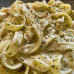 Fettuccine con pollo, decorado con albahaca y trozos de queso parmesano.