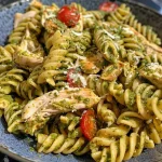 Pasta con pollo y tomates cherry decorada con albahaca fresca en un plato.