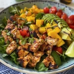 Vista lateral de una ensalada colorida con pollo a la parrilla y trozos de mango.