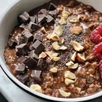 ['Tazón de avena de chocolate con frutas y chocolate oscuro.', 'Avena de chocolate en un tazón, decorada con plátano y frambuesas.', 'Detalle de una porción de avena de chocolate con nueces y frutas.', 'Avena de chocolate cremosa con trozos de chocolate y frutos frescos.']