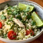 ['Tazón de arroz con cilantro y lima acompañado de pollo y vegetales.', 'Primer plano de un plato de arroz con pollo, cilantro y lima.', 'Receta de arroz con cilantro y lima presentada en un tazón con pollo.', 'Arroz con lima y pollo con toppings frescos como aguacate y tomate.']