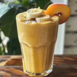 ['Smoothie de plátano y durazno en un vaso transparente.', 'Primer plano de un batido de plátano y durazno con hielo.', 'Vaso de smoothie cremoso de plátano y durazno sobre una mesa.', 'Batido de frutas de plátano y durazno con decoración fresca.']