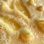 ['Mousse de jengibre en un tazón, con textura cremosa y color dorado.', 'Primer plano de mousse de jengibre, mostrando su superficie suave y su forma en el tazón.', 'Tazón con mousse de jengibre, evidenciando su delicada consistencia y color.', 'Mousse de jengibre presentada en un plato, con un fondo difuminado.']